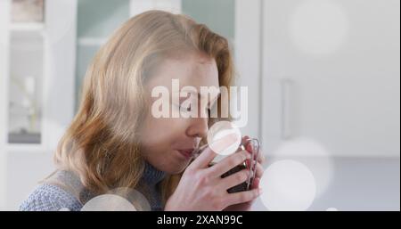 Immagine di una giovane donna caucasica che si gusta una bevanda calda, tenendo una tazza con entrambe le mani Foto Stock