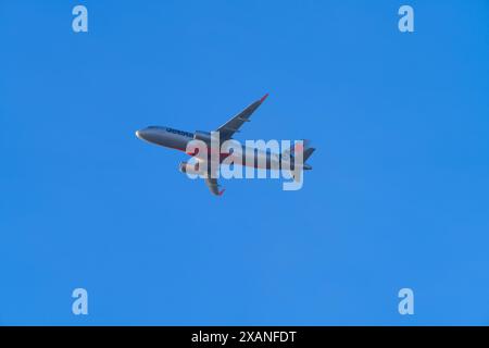 Un aereo Jetstar in volo con uno sfondo blu senza nuvole, Victoria, Australia. Foto Stock