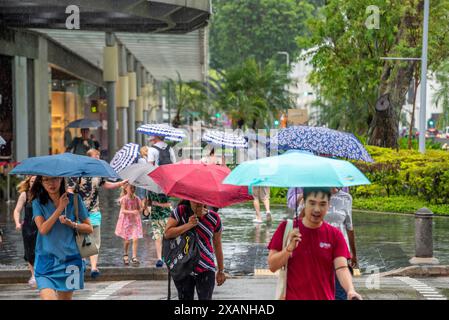 Gli amanti dello shopping e i turisti attraversano Stamford Road nella città di Singapore sotto la pioggia con ombrelli colorati Foto Stock