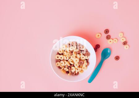 Anelli di mais senza latte in un piatto bianco su sfondo rosa con un cucchiaio blu Foto Stock