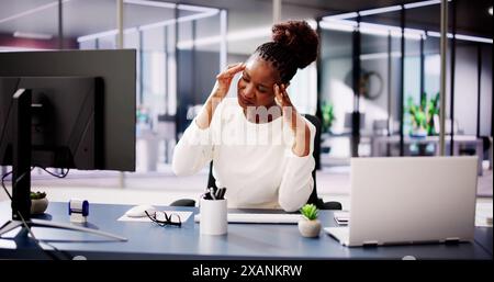 Donna d'affari stanca che lavora al computer in ufficio, combattendo lo stress e il mal di testa tra le responsabilità e le pressioni quotidiane. Foto Stock