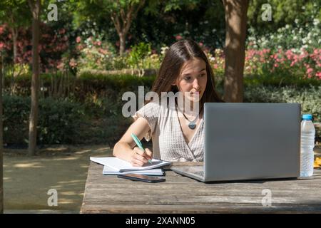 Attenta ragazza universitaria che prende appunti e usa il suo portatile a un tavolo del campus. Studente concentrato, inizio delle lezioni, tecnologia, vita accademica, istruzione Foto Stock