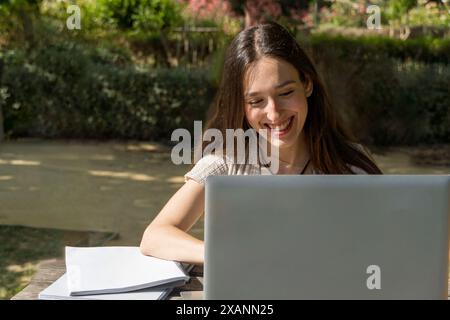 Studente universitario sorridente mentre usa il suo laptop nel campus all'inizio delle lezioni. Tecnologia, vita accademica, riunione virtuale, inizio del college Foto Stock