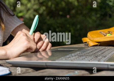 Mani di una giovane studentessa che prende appunti mentre usa il suo portatile all'aperto nel campus. Studente, inizio delle lezioni, tecnologia, vita accademica. Foto Stock