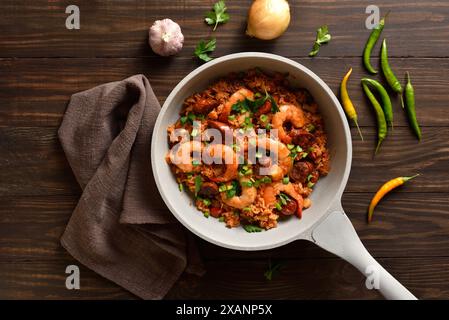 Jambalaya creola con gamberetti, salsicce affumicate e verdure in padella leggera su fondo in legno. Vista dall'alto, disposizione piatta Foto Stock