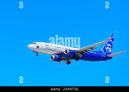 Los Angeles, California - 9 aprile 2024: Vista dal basso di un aereo Alaska Airlines che vola in alto nel cielo, evidenziata su uno sfondo blu brillante. Foto Stock