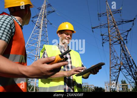 Elettricisti professionisti in uniformi vicino a torri ad alta tensione Foto Stock