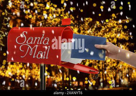 Donna che mette la lettera a Babbo Natale nella cassetta della posta sotto la neve che cade all'aperto, primo piano. Tradizione natalizia Foto Stock