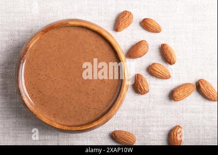 Marinare il burro di mandorle in una ciotola di legno su tessuto di lino. Pasta per alimenti liscia composta da mandorle triturate in burro di noci. Purea di noci di Prunus dulcis. Foto Stock