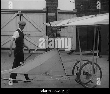 Maschio civile che trasporta una piccola macchina volante a pedale e cerca di dimostrarla in un parco ma fallisce, 1929. Perche' non un aereo in ogni garage - perche' non il giro aereo di ogni uomo? Qualcosa di piccolo, semplice ed economico... ogni volta che c'è bisogno, c'è sempre qualcuno che cerca di riempirlo... rideva di Leonardo da Vinci... in ogni campo dell'impegno umano, la speranza nasce eterna". Da "Time to Remember - 1929 The Time of the House at Bognor" - Reel 3; un documentario sul mondo nel 1929. Malattia di re Giorgio V &amp; depressione economica. Foto Stock