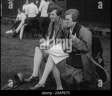 Due civili femminili che indossano uniformi scolastiche che prendono appunti su un blocco note a lato di un campo da gioco, anni 1920 Da "Time to Remember - Teenage Flapper", anni '1920 (Reel 1); un dcumentary sulla vita delle donne negli anni '1920 - grande commento di Joyce Grenfell. Foto Stock