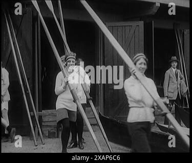 Giovani civili femminili che indossano abiti sportivi che trasportano lame di canottaggio in arrivo per una classe di canottaggio, anni '1920 Da "Time to Remember - Teenage Flapper", anni '1920 (Reel 2); un dcumentary sulla vita delle donne negli anni '1920 - grande commento di Joyce Grenfell. Foto Stock