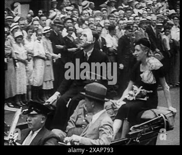 Folla che guarda Jim e Amy Mollison seduti in una macchina, 1933. '...a Broadway c'era più carta che pioggia. Tutti ne hanno avuto un bel calcio". Il 22 luglio 1933, gli aviatori britannici Jim Mollison e Amy Johnson decollarono dal Galles del Sud con un volo non-stop per New York, ma furono costretti ad atterrare a Bridgeport, Connecticut, poco prima del loro obiettivo, dopo aver esaurito il carburante. Sono rimasti entrambi feriti, e l'aereo è stato rotto dai cercatori di souvenir. Da Time to Remember - The Time of the Monster, 1933 (Reel 2); film documentario sugli eventi del 1933, Rise of Roosevelt e Hitle Foto Stock