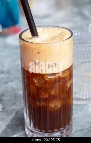 Primo piano di un caffè freddo ricoperto di schiuma e servito in un bicchiere alto con una cannuccia, perfetto per una giornata calda. Foto Stock