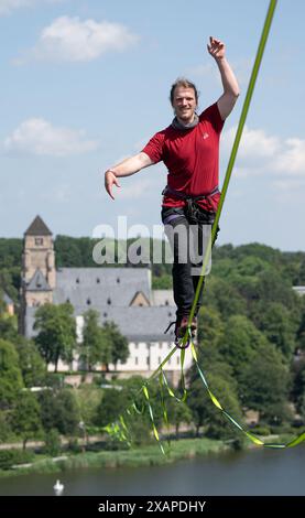 8 giugno 2024, Sassonia, Chemnitz: Jens Decke si bilancia fino a 50 metri di altezza su un'altura sopra il laghetto del castello di Chemnitz. La linea lenta lunga 630 metri si estende tra la torre della chiesa del castello (sul retro) e un alto edificio ed è considerata la linea più lunga in un'area urbana della Germania. Gli slackliner impiegano poco meno di 45 minuti in un solo tratto. La linea abbraccia le basi del festival della democrazia "Kosmos”. Secondo gli organizzatori, un totale di oltre 200 voci del programma saranno offerte in un giorno. Sono previsti circa 50.000 visitatori per partecipare al festival. Foto Foto Stock