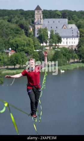 8 giugno 2024, Sassonia, Chemnitz: Jens Decke si bilancia fino a 50 metri di altezza su un'altura sopra il laghetto del castello di Chemnitz. La linea lenta lunga 630 metri si estende tra la torre della chiesa del castello (sul retro) e un alto edificio ed è considerata la linea più lunga in un'area urbana della Germania. Gli slackliner impiegano poco meno di 45 minuti in un solo tratto. La linea abbraccia le basi del festival della democrazia "Kosmos”. Secondo gli organizzatori, un totale di oltre 200 voci del programma saranno offerte in un giorno. Sono previsti circa 50.000 visitatori per partecipare al festival. Foto Foto Stock