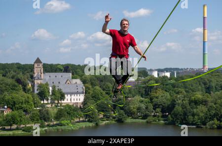 8 giugno 2024, Sassonia, Chemnitz: Jens Decke si bilancia fino a 50 metri di altezza su un'altura sopra il laghetto del castello di Chemnitz. La linea lenta lunga 630 metri si estende tra la torre della chiesa del castello (sul retro) e un alto edificio ed è considerata la linea più lunga in un'area urbana della Germania. Gli slackliner impiegano poco meno di 45 minuti in un solo tratto. La linea abbraccia le basi del festival della democrazia "Kosmos”. Secondo gli organizzatori, un totale di oltre 200 voci del programma saranno offerte in un giorno. Sono previsti circa 50.000 visitatori per partecipare al festival. Foto Foto Stock