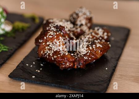 Ali di pollo in salsa al miele di soia con semi di sesamo su un bordo nero Foto Stock