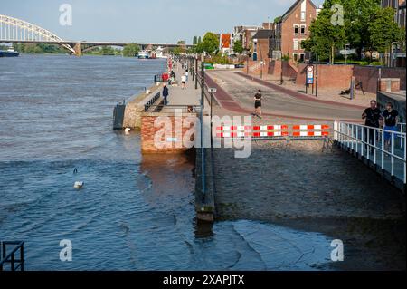 Si vedono persone passare davanti a un'area allagata. Le persistenti piogge nella Germania meridionale stanno causando un aumento del livello dell'acqua nella zona olandese vicino alla Germania. d. nella città di Lobith, al confine con la Gheldria, è stato misurato un livello di 12,85 metri sopra il piano nazionale di pesca (la base utilizzata per misurare il livello dell'acqua). A Nijmegen, parti basse della banchina e intorno al porto di Waalkade sono sott'acqua. Il livello dell'acqua del Reno ha raggiunto un picco il venerdì mattina, ma era meno alto di quanto inizialmente previsto. L'aspettativa era che l'acqua salisse a più di 13 metri sopra NAP. (Foto di Ana Ferna Foto Stock