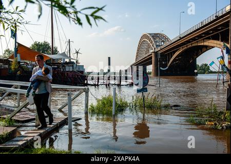 Si vede un uomo che porta il suo bambino in un'area allagata. Le persistenti piogge nella Germania meridionale stanno causando un aumento del livello dell'acqua nella zona olandese vicino alla Germania. d. nella città di Lobith, al confine con la Gheldria, è stato misurato un livello di 12,85 metri sopra il piano nazionale di pesca (la base utilizzata per misurare il livello dell'acqua). A Nijmegen, parti basse della banchina e intorno al porto di Waalkade sono sott'acqua. Il livello dell'acqua del Reno ha raggiunto un picco il venerdì mattina, ma era meno alto di quanto inizialmente previsto. L'aspettativa era che l'acqua salisse a più di 13 metri sopra NAP. Foto Stock