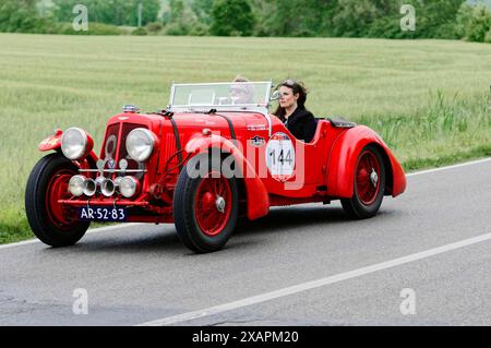 Auto da corsa classica rossa su una strada di campagna in un paesaggio verde con due piloti, il cielo è blu, auto d'epoca, corsa automobilistica, mille miglia, 1000 miglia Foto Stock