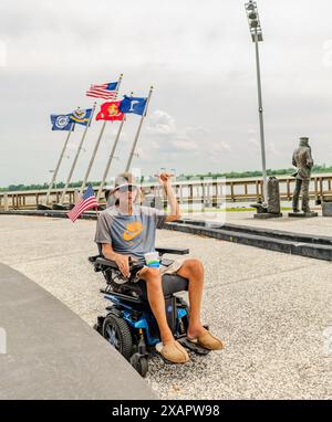 Charleston, South Carolina: Veterano disabili seduto sulla sedia a rotelle con il pugno in alto con le bandiere nel museo Navy Yard di Charleston Foto Stock