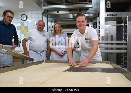 Allstedt, Germania. 8 giugno 2024. Vincent Richter (r) della panetteria MEye posiziona l'impasto del lievito alla base della torta di semi di papavero più grande del mondo nel vassoio da forno gigante appositamente realizzato Il tentativo record è una campagna della Saxony-Anhalt Art Foundation per celebrare l'anno commemorativo '500 anni della guerra dei contadini e il 500 ° anniversario della morte di Thomas Müntzer nel 2025. Müntzer tenne il suo famoso sermone al castello di Allstedt nel 1524. Crediti: Heiko Rebsch/dpa/Alamy Live News Foto Stock