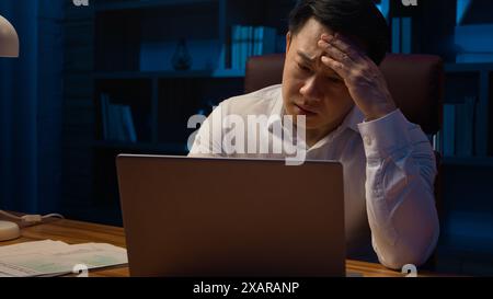 Asiatico stressato uomo coreano stanco di mezza età stanco affaticato uomo d'affari sovraccarico di lavoro dei computer portatili problemi di lavoro di ufficio documenti risultati cattivi documenti Foto Stock