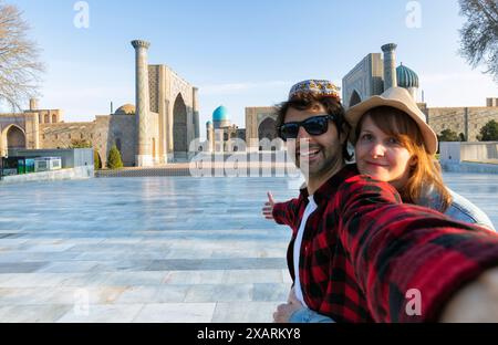 Coppia felice di turisti che fanno un selfie con Registan come sfondo nella città di Samarcanda, Uzbekistan, Asia centrale Foto Stock