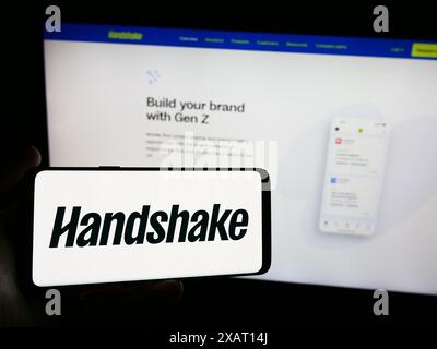 Persona con smartphone e logo della società di software per il reclutamento statunitense Stryder Corp. (Handshake) davanti al sito Web. Mettere a fuoco il display del telefono. Foto Stock