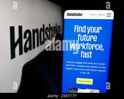 Persona che detiene un cellulare con pagina Web della società di software per il reclutamento statunitense Stryder Corp. (Handshake) con logo. Messa a fuoco al centro del display del telefono. Foto Stock