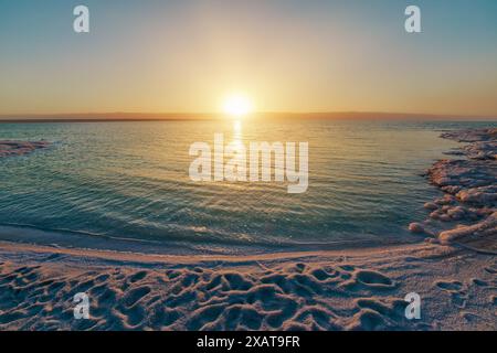 Vista mozzafiato di un tranquillo tramonto che si riflette sulle tranquille acque giordane del Mar morto in Giordania, con formazioni saline Foto Stock