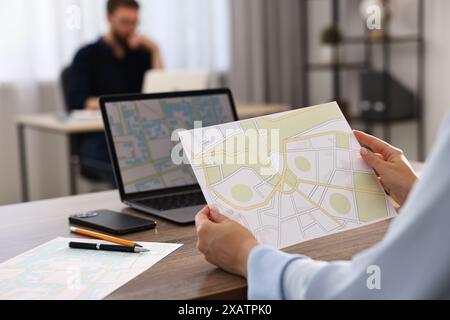 Cartografo che lavora con mappe catastali al tavolo di legno in ufficio, primo piano Foto Stock