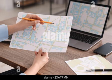 Cartografo che lavora con mappe catastali al tavolo di legno in ufficio, primo piano Foto Stock