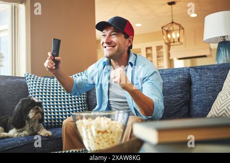 Happy, uomo e cane con telecomando per la tv o popcorn a casa sul divano per guardare le partite sportive, le sfide e il divertimento. Soggiorno, divano e divertimento o sorrisi Foto Stock