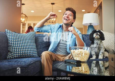 Eccitato, uomo e festeggiamenti guardando la tv o popcorn a casa sul divano con giochi sportivi, sfide e divertimento. Soggiorno, divano e sorriso o felice Foto Stock