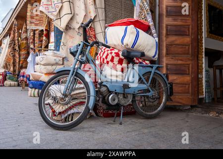 Un piccolo vecchio ciclomotore blu tipico è parcheggiato appoggiato su un negozio di tessuti in una strada nella Kasbah delle Oudayas a Rabat, capitale del Marocco Foto Stock