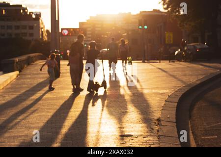 Scena urbana astratta. Sagome di persone nella luce calda che camminano lungo una strada al tramonto. Ombre lunghe su un terreno. Il sole tramonta all'alba. Foto Stock