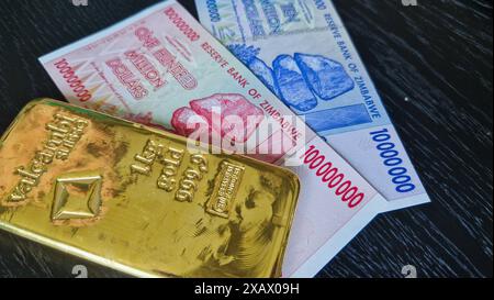 Stoccolma, Svezia - 15 maggio 2024: Banconote da cento milioni di dollari e dieci milioni di dollari dello Zimbabwe con lingotto d'oro. Foto Stock