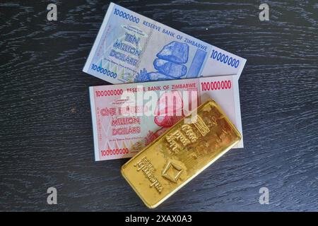 Stoccolma, Svezia - 15 maggio 2024: Banconote da cento milioni di dollari e dieci milioni di dollari dello Zimbabwe con lingotto d'oro. Foto Stock