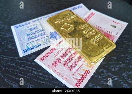 Stoccolma, Svezia - 15 maggio 2024: Banconote da cento milioni di dollari e dieci milioni di dollari dello Zimbabwe con lingotto d'oro. Foto Stock