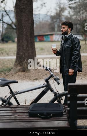 Uomo d'affari che fa una pausa in un parco con la sua bicicletta e il caffè Foto Stock