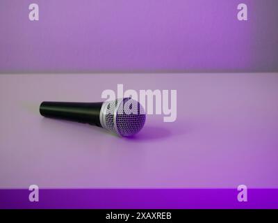 Un microfono professionale per la registrazione o lo streaming audio si trova su un tavolo bianco con luce al neon viola. Foto Stock