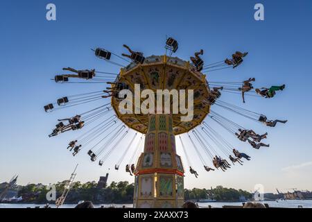 Gröna Lund sull'isola museo di Djurgården è il più antico parco divertimenti della Svezia ed è stato fondato nel 1883 dal tedesco Jacob Schultheiss. Il parco divertimenti è diviso in una parte vecchia e una nuova. Qui la giostra a catena nostalgica al sole della sera. Si trova direttamente sull'acqua. Carosello a catena a Gröna Lund Tivoli. Parco divertimenti stagionale con montagne russe e giostre emozionanti, giochi competitivi e concerti dal vivo. Djurgårdsstaden, Stoccolma, Svezia Foto Stock