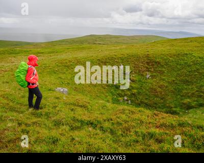 Un camminatore che guarda un grande buco di scuotimento o un lavandino sulla Black Mountain nel Brecon Beacons Bannau Brycheiniog nel Galles del Sud nel Regno Unito Foto Stock