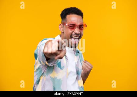 Giovane ragazzo nero emotivo in un ambiente informale che rialza la scena dello studio, celebra il successo, felice e affascinante uomo millenario afroamericano che condivide buone emozioni. Foto Stock