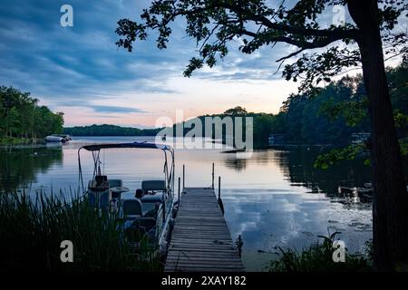 Si affaccia su un lago del Wisconsin mentre l'ultima luce del giorno svanisce. Barca legata al molo. Un altro pesce con le luci accese. Foto Stock