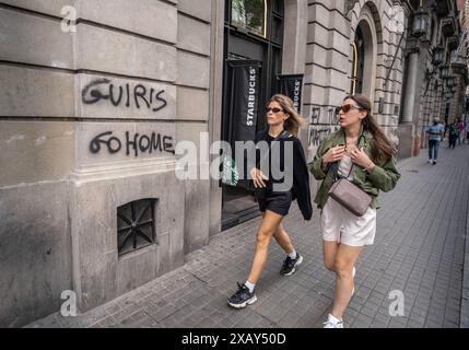 Barcellona, Spagna. 9 giugno 2024. Una giovane coppia di turisti si vede passare davanti ai graffiti anti-turismo. Come la maggior parte delle capitali europee, Barcellona vive tra la necessità di un'economia del turismo di cui non può fare a meno e il rifiuto di un ampio gruppo di cittadini contro la distorsione culturale e l'insicurezza occupazionale tipica del settore turistico. Gli slogan sugli spazi pubblici dell'ultima manifestazione contro il sovraffollamento turistico coesistono con un'attività turistica che non riposa mai. (Foto di Paco Freire/SOPA Images/Sipa USA) credito: SIPA USA/Alamy Live News Foto Stock