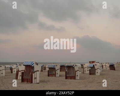 Sdraio vuote sulla spiaggia sotto un cielo serale leggermente nuvoloso e un tramonto di colore arancione, Spiekeroog, Frisia orientale, GERMANIA Foto Stock