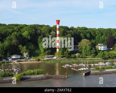 Faro sulla riva del fiume, circondato da alberi, con diverse barche ed edifici sullo sfondo, Amburgo, Germania Foto Stock